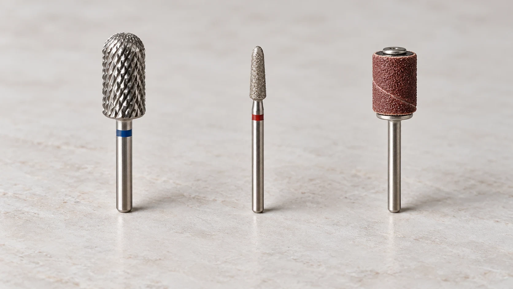 Three nail drill tools shown side by side: a barrel bit, a detail bit, and a sanding band on a mandrel